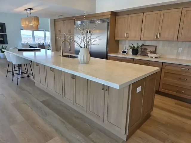Kitchen by Better Remodels with light wood cabinets, a long island with a white stone top and wood-look plank floors
