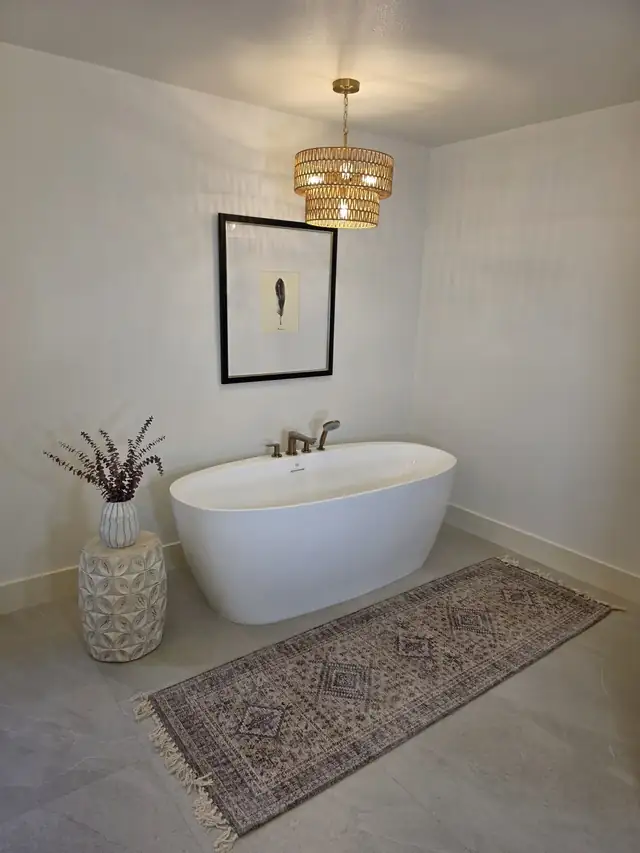 Bathroom by Better Remodels with a freestanding white tub, a gold chandelier and gray tile floors