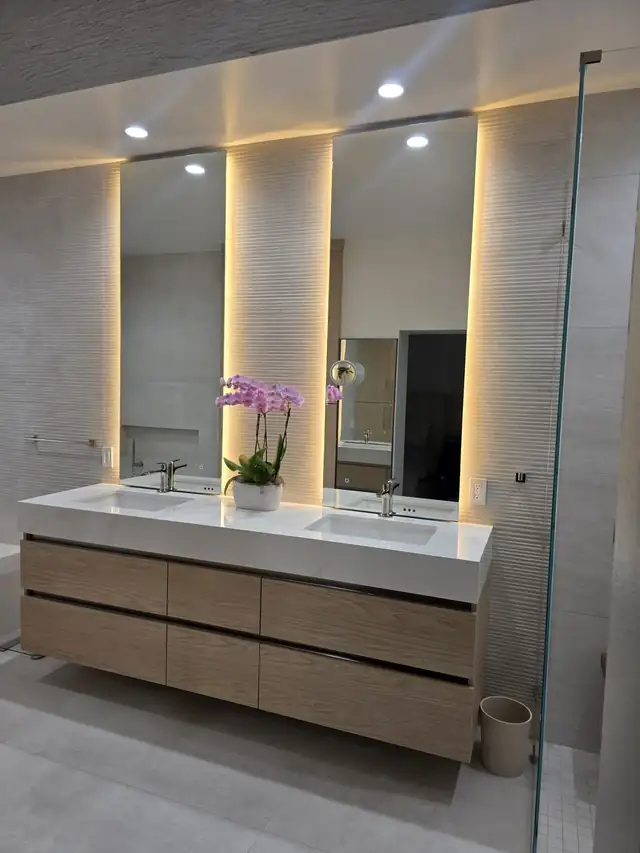 Bathroom remodel with a floating wood vanity, two white sinks and tall backlit mirrors