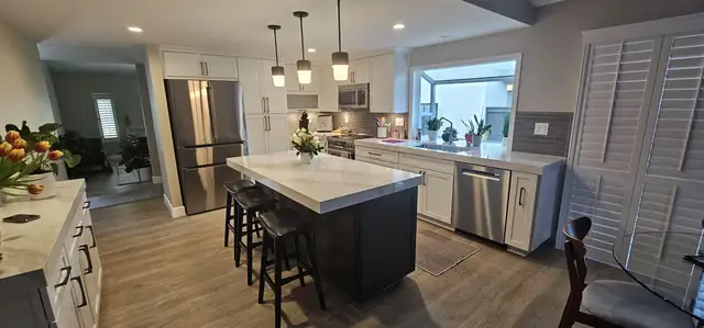 Open kitchen remodel with a navy island, white quartz top, pendant lights and new wood-look flooring