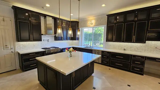 Kitchen remodel with black cabinets, a large white-topped island, glass pendants and under-cabinet lighting