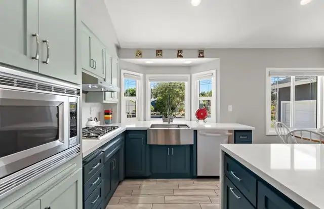 Santa Ana home remodel kitchen with pale sage upper cabinets, navy lower cabinets, a farmhouse sink and white counters